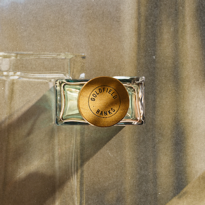 Top view of a luxury fragrance bottle with a gold cap in natural light on a neutral textured background