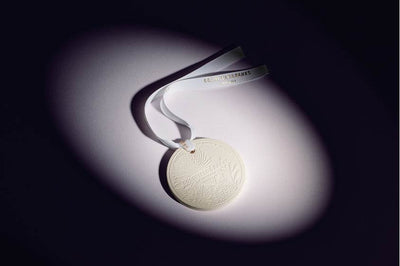 Mystic Bliss scented round ceramic ornament with white ribbon on dark background